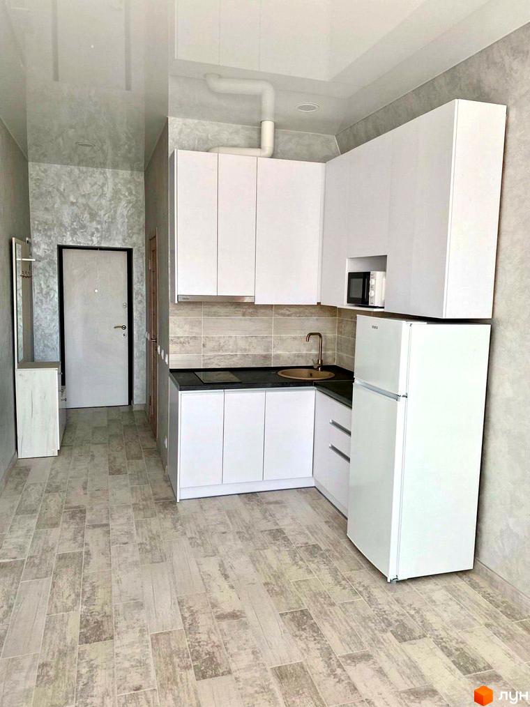 Кухня з білими шафами та холодильником у ЖК Сузір'я 2020. Інтер'єр новобудови з сірими стінами та підлогою.