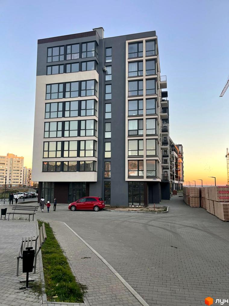 Зображення фасаду Новобудови Kokos Avenue. Багатоповерховий будинок з великими вікнами та червоним авто на прибудинковій території.