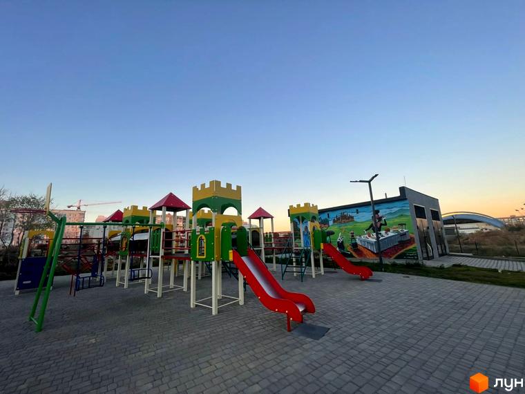 Зображення дитячого майданчика біля Новобудови Kokos Avenue. Майданчик з гірками та ігровими елементами.
