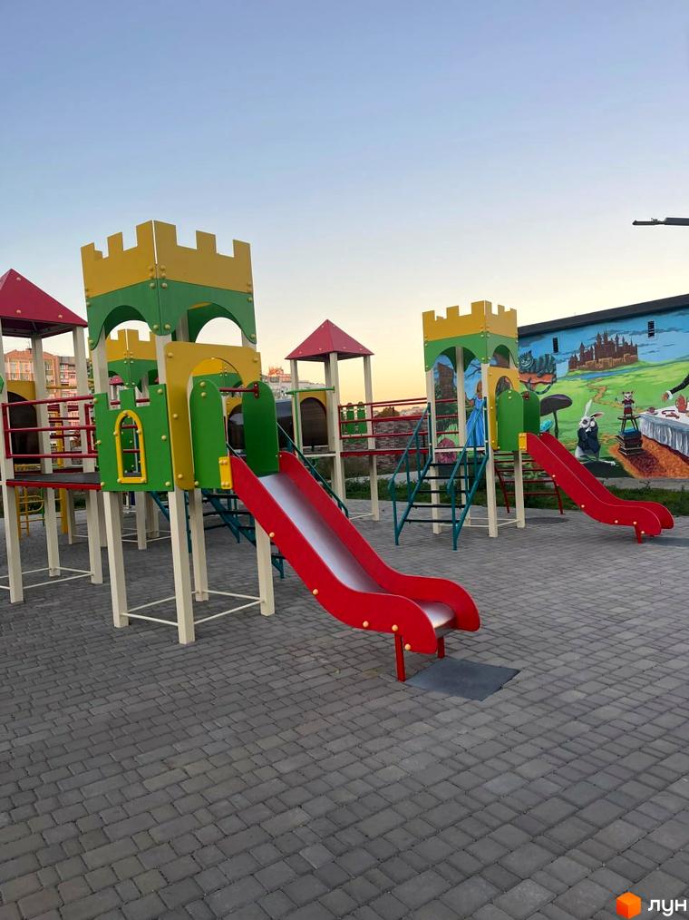 Дитячий майданчик з гірками та вежами у Житловому комплексі Kokos Avenue. Ігровий комплекс з червоними та жовто-зеленими елементами.