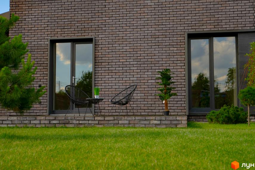 Зовнішній вигляд будинку КМ BritanHouse з цегляним фасадом та великими вікнами. Прибудинкова територія з доглянутим газоном та зеленими насадженнями.