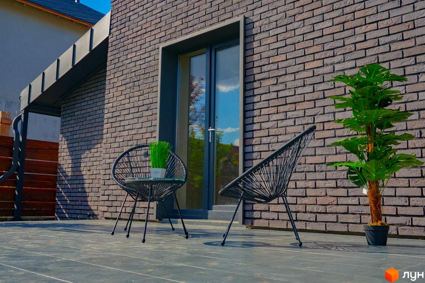 Котеджне містечко BritanHouse з цегляним фасадом та зоною відпочинку на терасі. Навколо будинку зелені насадження та облаштована прибудинкова територія.