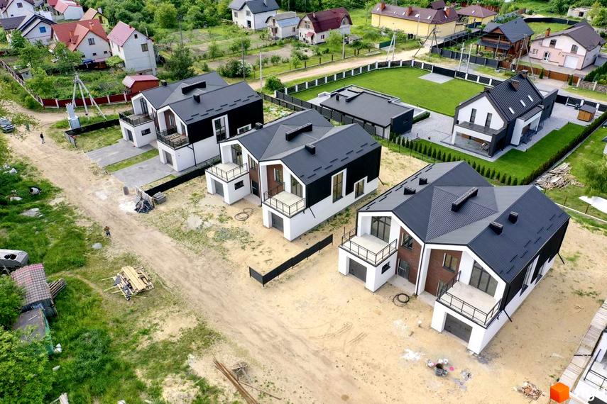 Дуплекси Черешня: сучасні двоповерхові будинки з чорними дахами та білими фасадами, розташовані на піщаній ділянці з зеленою травою та деревами.