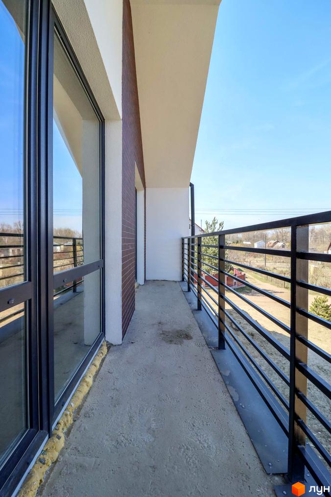 Балкон з панорамними вікнами та чорною огорожею в Дуплексах „Черешня“. Вид на вулицю з приватними будинками.