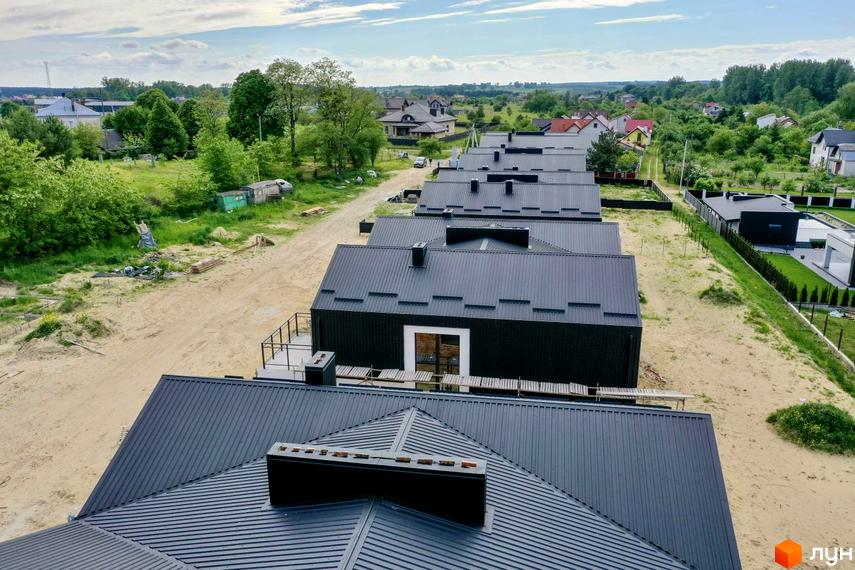 Дуплекси „Черешня“: сучасні будинки з темними металевими дахами та фасадами, розташовані на піщаній ділянці з зеленою зоною навколо.