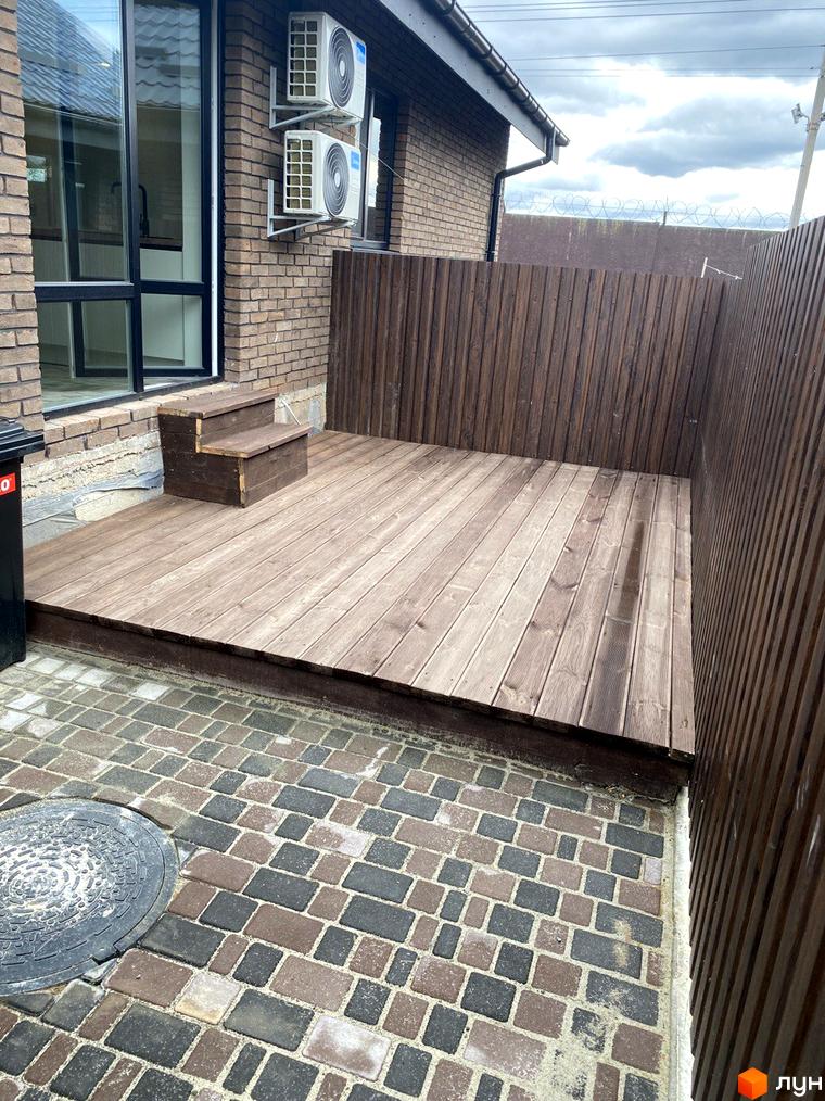 Котеджне містечко Панська Баварія: цегляний будинок з дерев'яною терасою та вимощеною плиткою прибудинковою територією.