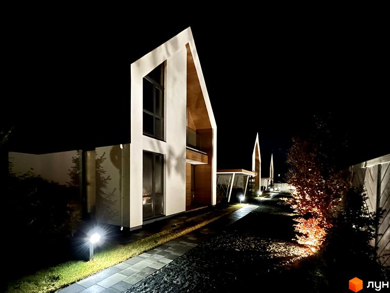 Котеджне містечко КМ Hill Park: двоповерхові будинки з дерев'яними елементами та підсвіткою в темний час доби. Навколо будівель — доглянута територія з доріжками та освітленням.