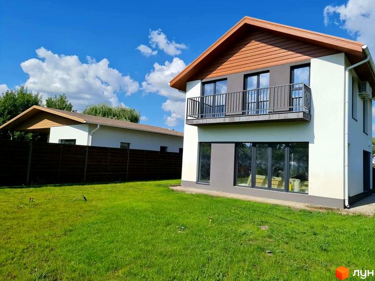Котеджне містечко Заміський: двоповерховий будинок з балконом та великими вікнами, зелений газон та дерев'яний паркан. Заміський комплекс з доглянутою територією під блакитним небом.