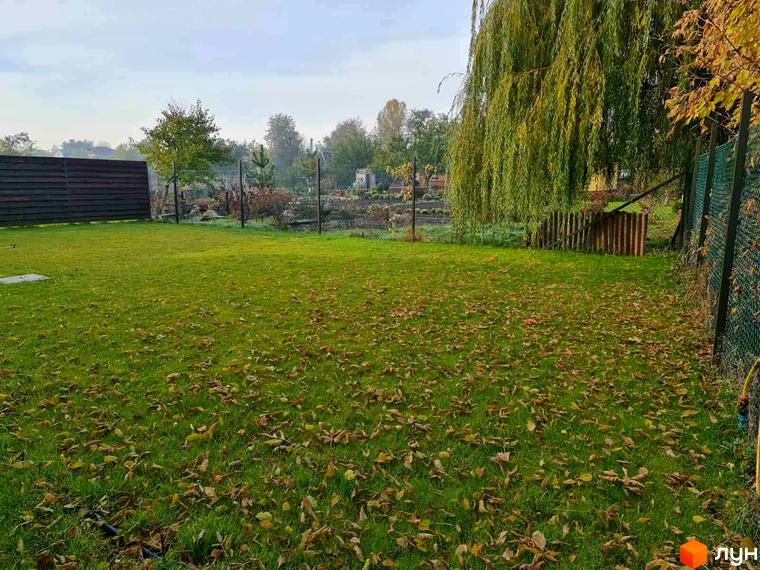 Котеджне містечко Заміський: зелений газон з опалим листям, паркан та велике дерево звисаюче над територією.