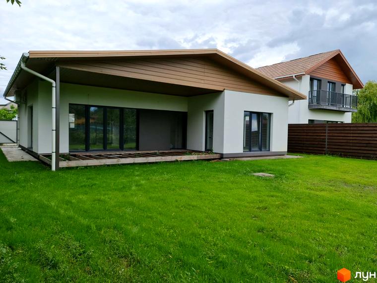 Котеджне містечко КМ Заміський: одноповерховий білий будинок з коричневим дахом та великими вікнами, зелена галявина перед ним.