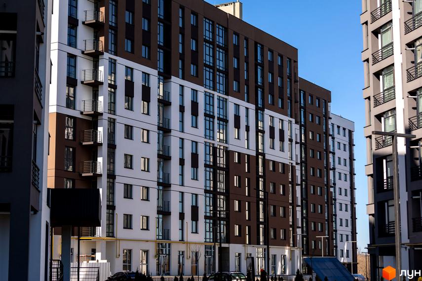 Фасад житлового комплексу Супернова з коричневими та білими секціями, балконами та великими вікнами. Перед будинком видно прибудинкову територію з деревами та автомобілями.