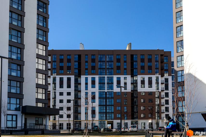 Новобудова ЖК Супернова з коричнево-білим фасадом та численними вікнами. На прибудинковій території видно дерева та лавки.