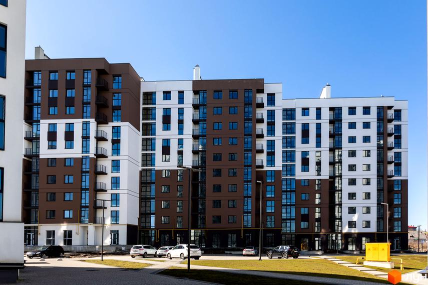 Новобудова ЖК Супернова з коричнево-білим фасадом та численними вікнами. Навколо будинку розташовані зелені газони та паркувальні місця з автомобілями.