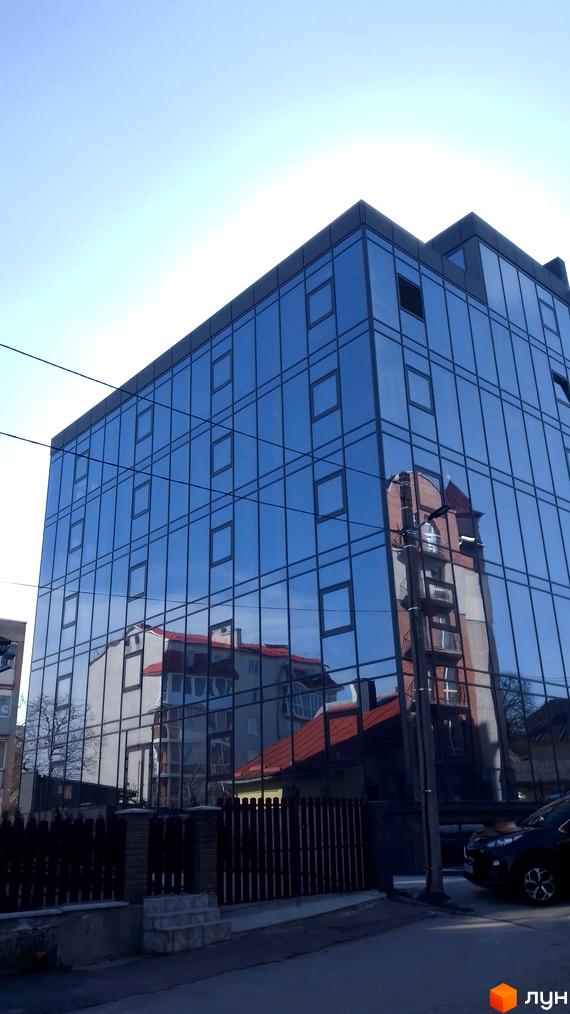 Сучасна новобудова на вулиці Петриківській, 9, з великою площею скління, що відбиває сусідні будівлі та небо. Перед будинком розташована огорожа та доглянута прибудинкова територія.