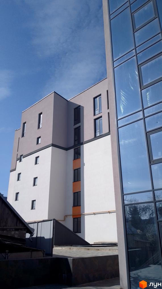 Фасад житлового комплексу на вулиці Петриківській, 9, з панорамним склінням та сірими і білими елементами. Навколо видно прибудинкову територію з елементами благоустрою.