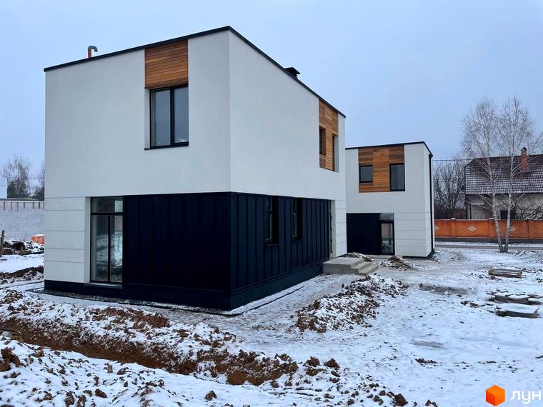 Котеджне містечко КМ 10 Families. Зовнішній вигляд двоповерхових будинків з білим фасадом, чорною цокольною частиною та дерев'яними елементами. Навколо будівельний майданчик зі снігом.