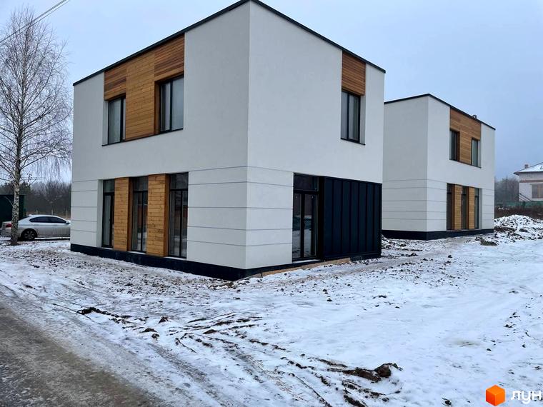 Зображення двоповерхового будинку в Котеджному містечку 10 Families з оздобленням фасаду деревом та великими вікнами. Навколо сніг.