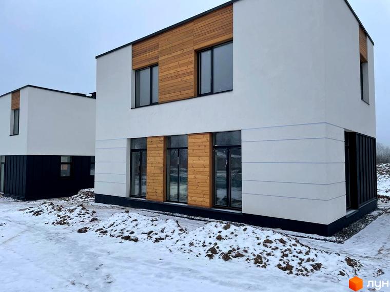 Зображення будинку в Котеджному містечку 10 Families. Двоповерховий будинок з дерев'яним оздобленням та великими вікнами на тлі снігу.