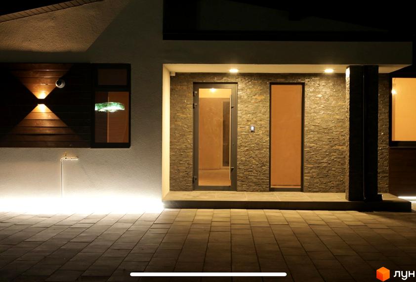 Житловий комплекс на вул. Мазепи: фасад будинку з кам'яним облицюванням, дерев'яною панеллю та освітленням. Прибудинкова територія вимощена плиткою з підсвічуванням.