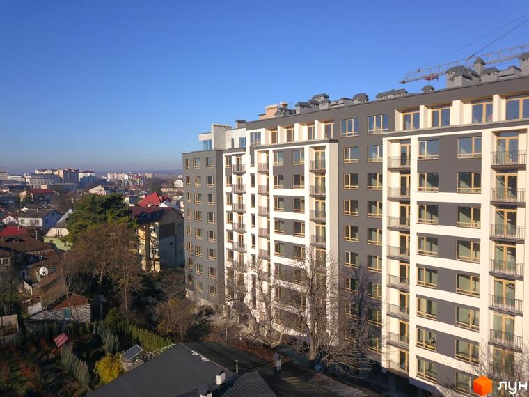 Висотна будівля ЖК Імперія з великою кількістю вікон та балконів на тлі міської забудови. Навколо будинку видно дерева та зелені насадження.