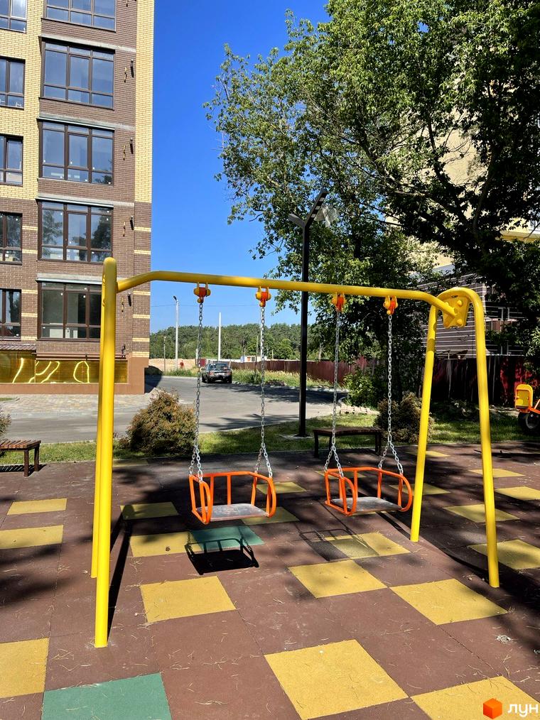 Житловий комплекс Масани: цегляний будинок з коричневими вікнами та дитячий майданчик з гойдалками на прибудинковій території.