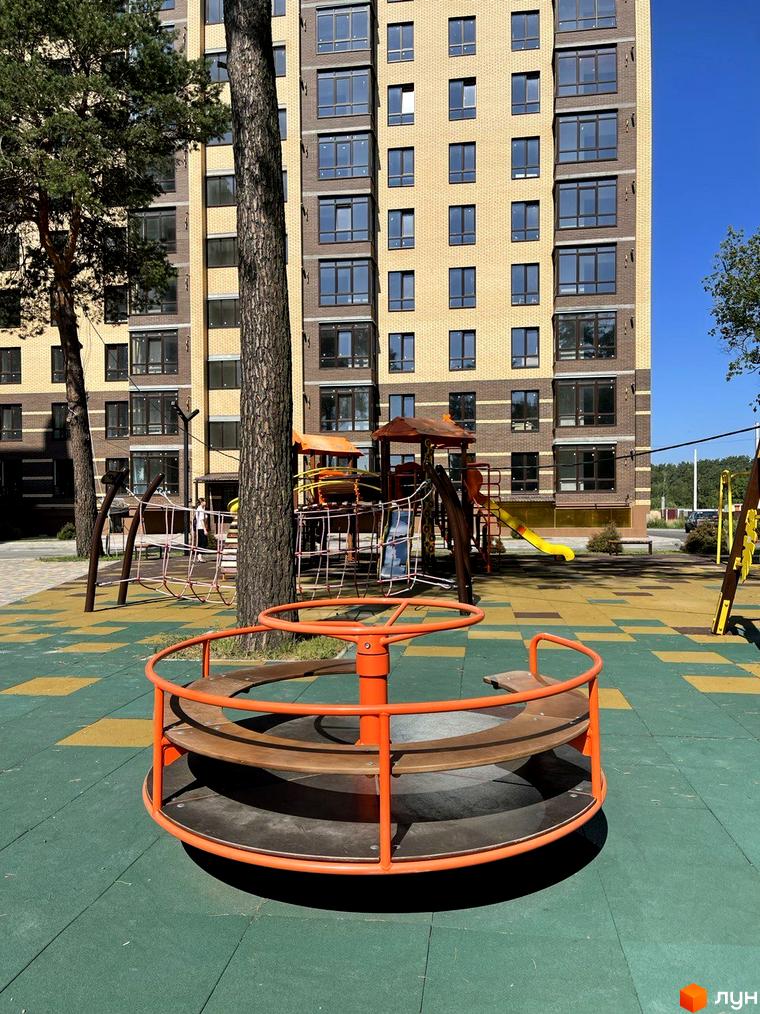 Житловий комплекс Масани: цегляний будинок з великими вікнами та дитячим майданчиком з каруселлю.