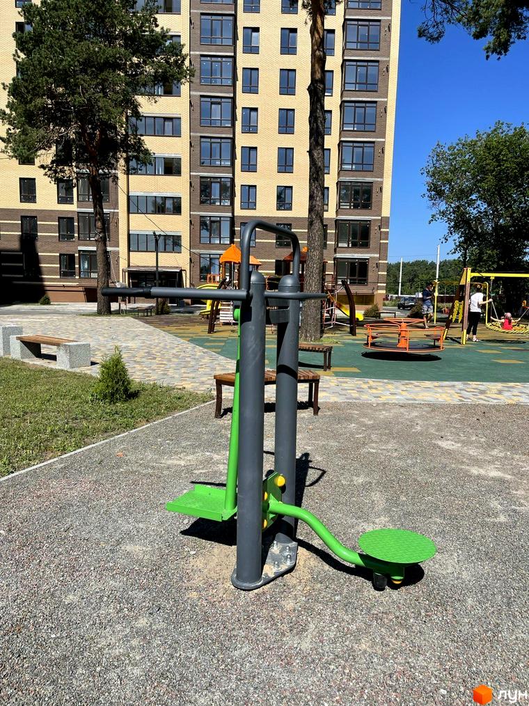 Новобудова ЖК Масани: цегляний фасад з великими вікнами, дитячий майданчик з гойдалками та спортивним тренажером.