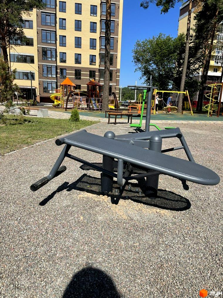 Новобудова ЖК Масани з дитячим майданчиком та спортивним обладнанням на прибудинковій території. Будинок має цегляний фасад та великі вікна.