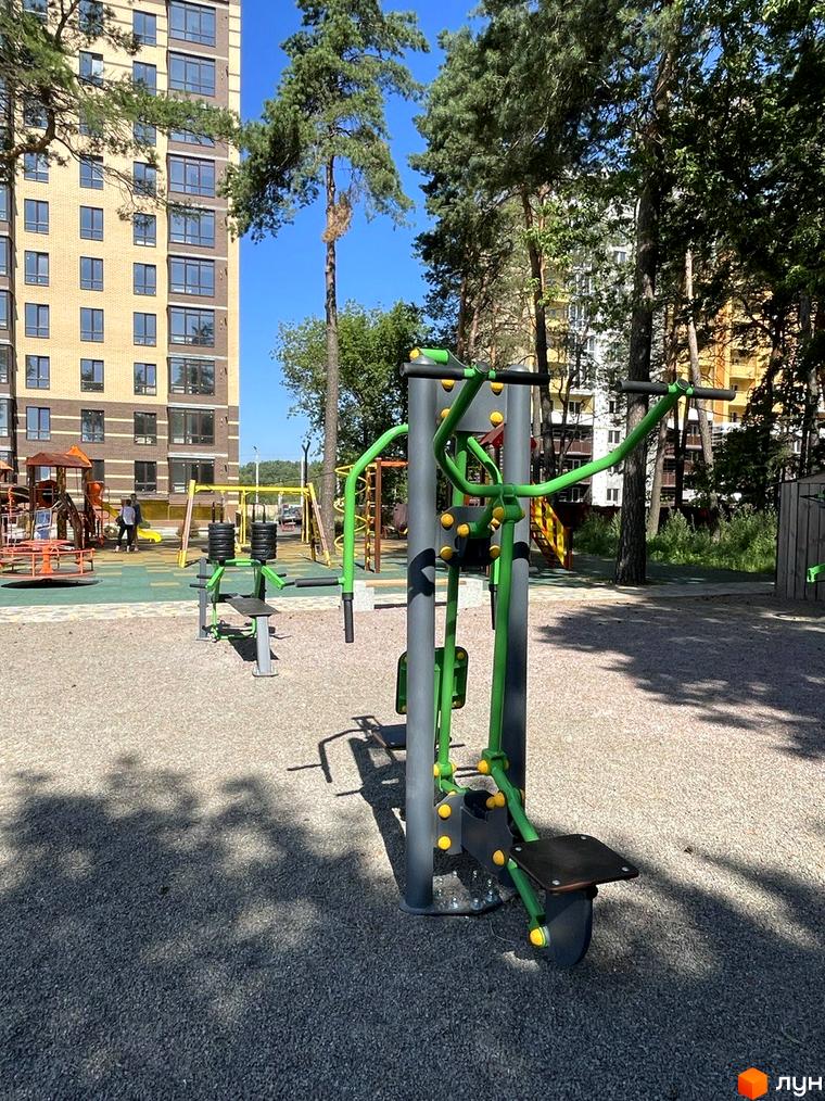 Житловий комплекс Масани: багатоповерховий будинок з жовтою цегляною обробкою та дитячим майданчиком з тренажерами на прибудинковій території.