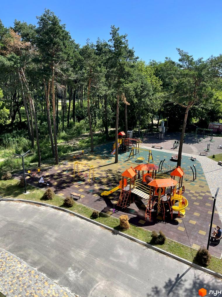 Дитячий майданчик з гірками та гойдалками на території житлового комплексу Масани. Зелена зона з деревами та місцями для відпочинку.