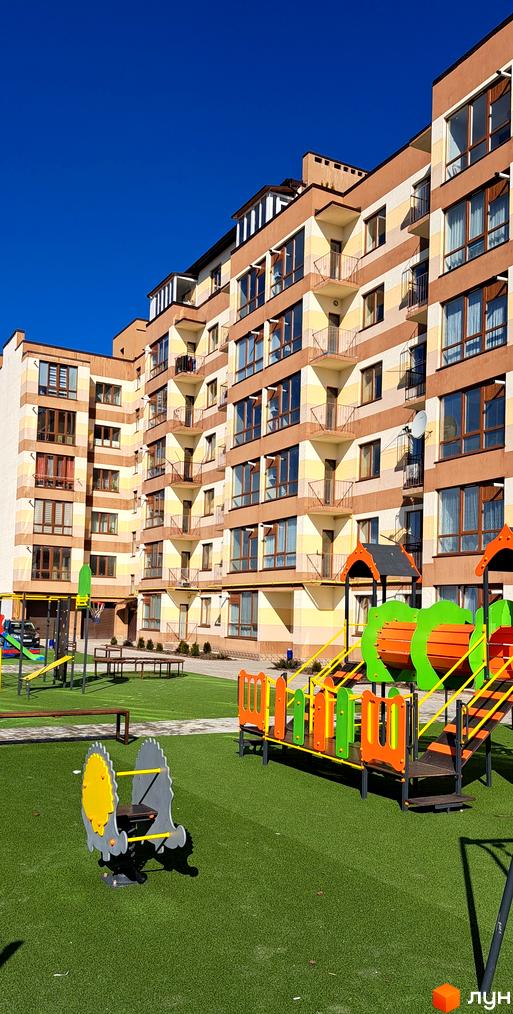 Житловий комплекс Мрія Золочів з фасадом у бежево-коричневих смугах та балконами. На прибудинковій території розташований дитячий майданчик.