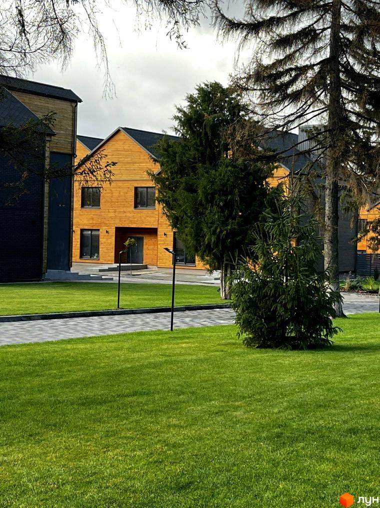 Котеджне містечко КМ Comfort City Lagoon. Фасади будівель оздоблені дерев'яними панелями та темною цеглою, навколо доглянутий газон та доріжки.