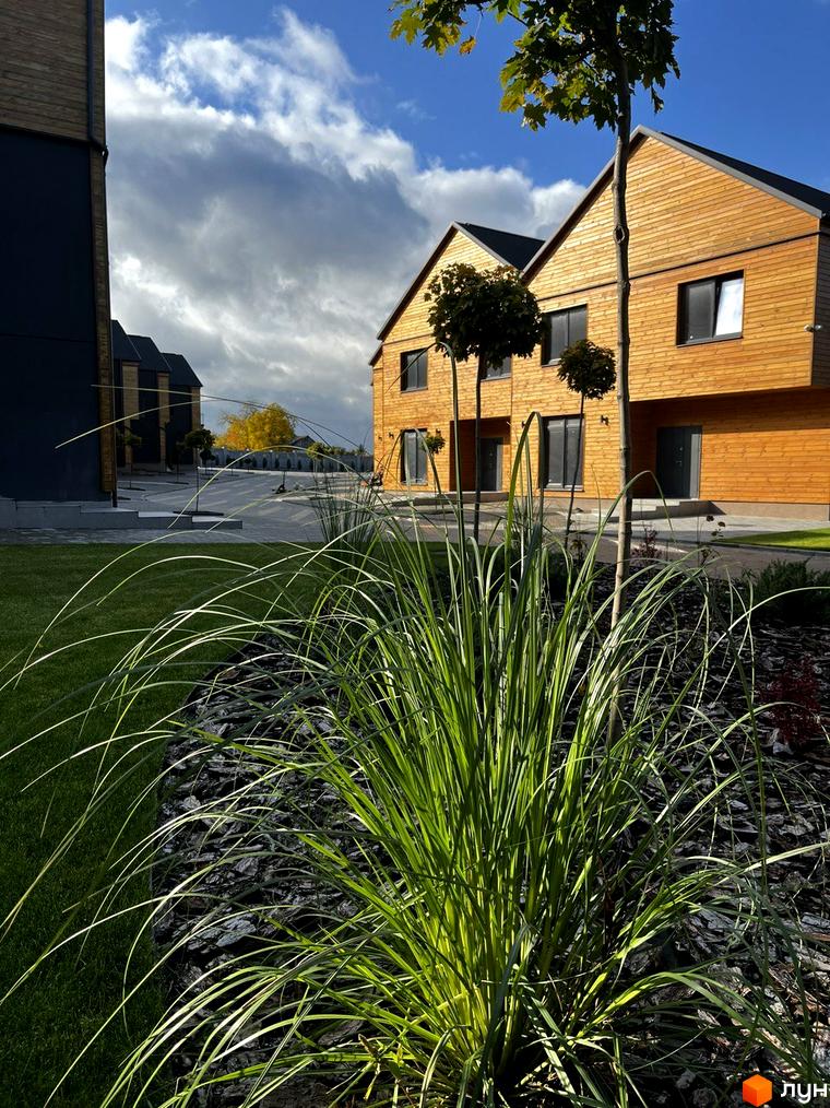 Котеджне містечко КМ Comfort City Lagoon з дерев'яним фасадом та доглянутою прибудинковою територією з газоном та декоративними рослинами.