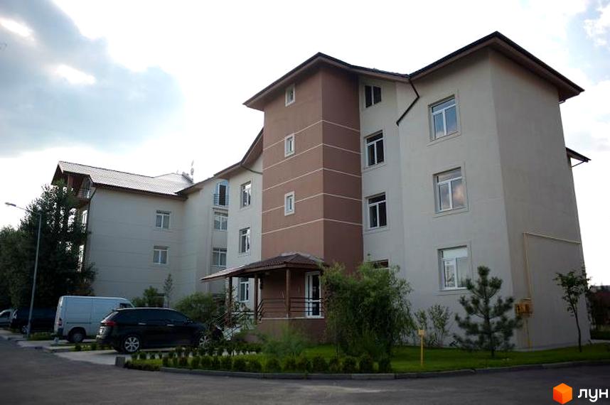 Житловий комплекс Бірюза - багатоповерховий будинок світло-бежевого кольору з коричневою вежею, вікна прямокутні. Навколо будинку зелена прибудинкова територія з деревами та кущами, парковка з автомобілями.