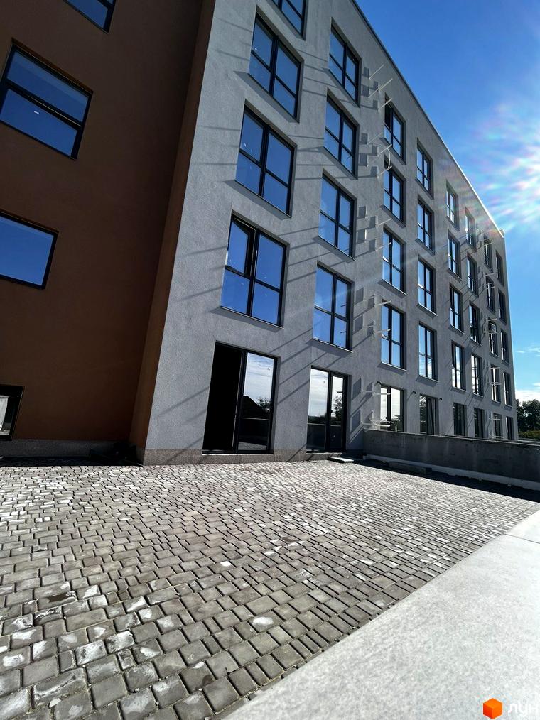 Будівельний проєкт Comfort City Lagoon з сірими та коричневими фасадами та великими вікнами. Перед будинком розташована бруківка.