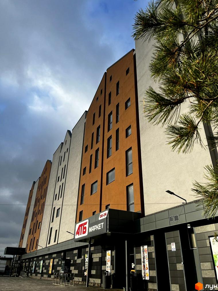 Новобудова ЖК Comfort City Lagoon з помаранчевими та білими фасадами, вікнами та вивіскою магазину АТБ МАРКЕТ.