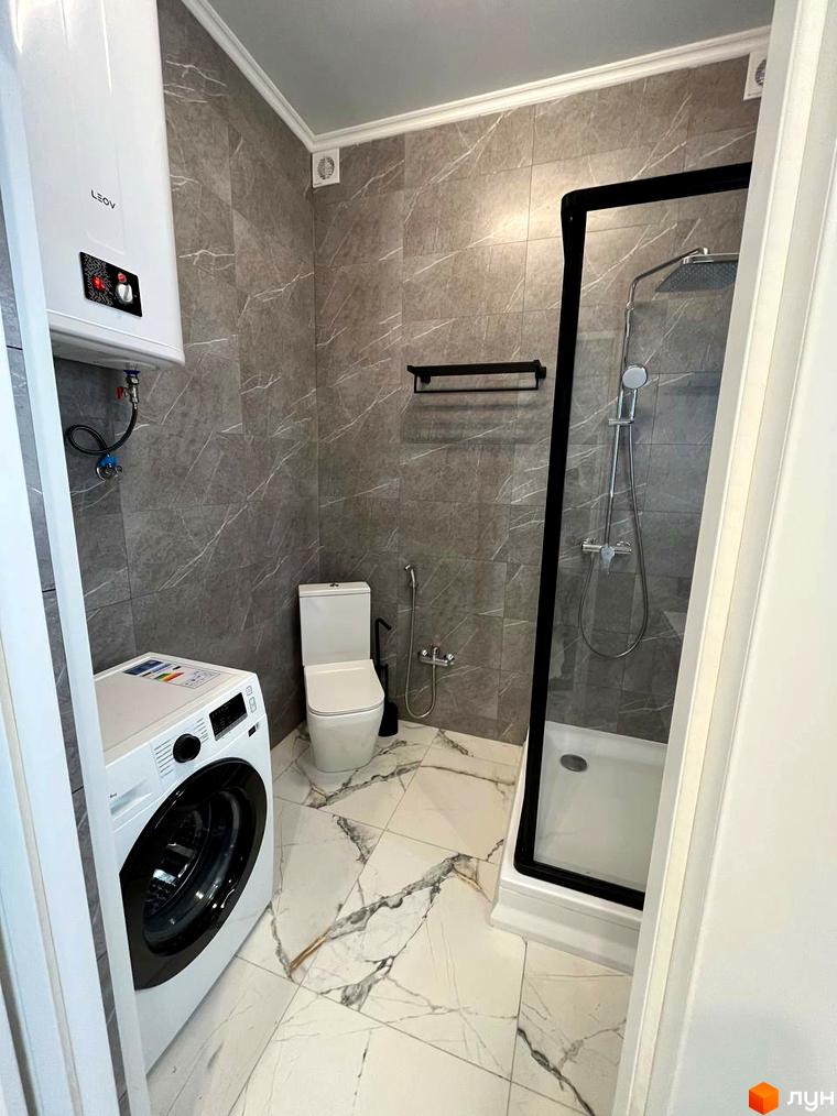 Сучасний санвузол з душовою кабіною та пральною машиною в ЖК Лелека. Оздоблення стін та підлоги виконано плиткою з мармуровим візерунком.