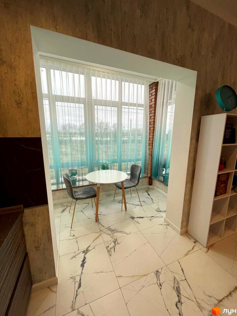 Інтер'єр квартири в ЖК Лелека з круглим столом, двома стільцями та великим вікном з видом на вулицю. Світлий простір з білою підлогою.