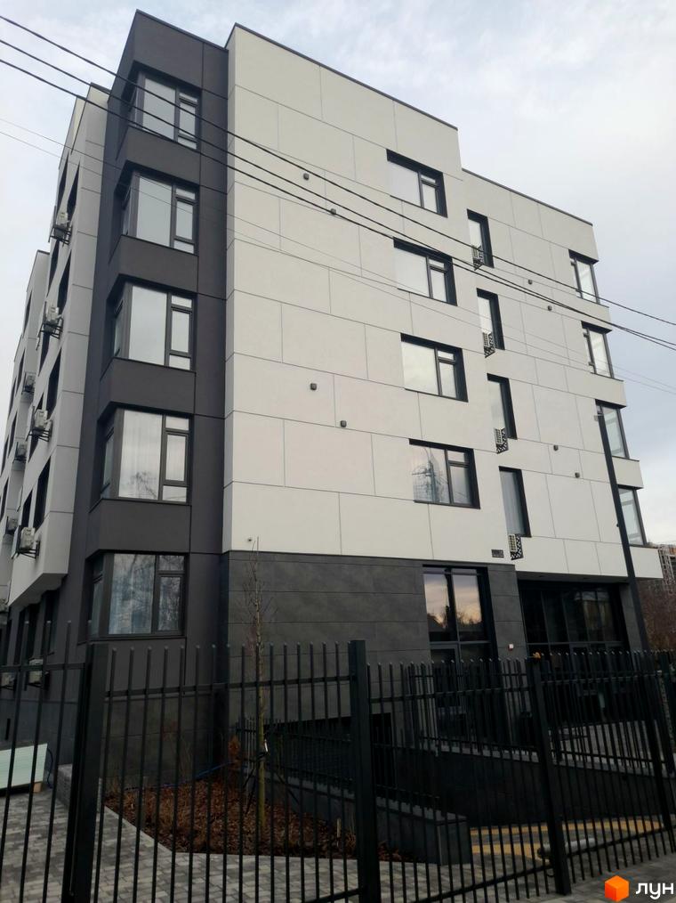 Будівельний проєкт ONYX sweet home з сірими та білими фасадами та великими вікнами. Навколо будинку чорний металевий паркан та зелені насадження.