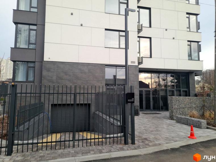 Фасад житлового комплексу ONYX sweet home з сірими та білими панелями, великими вікнами та огороженою прибудинковою територією з гаражними воротами.