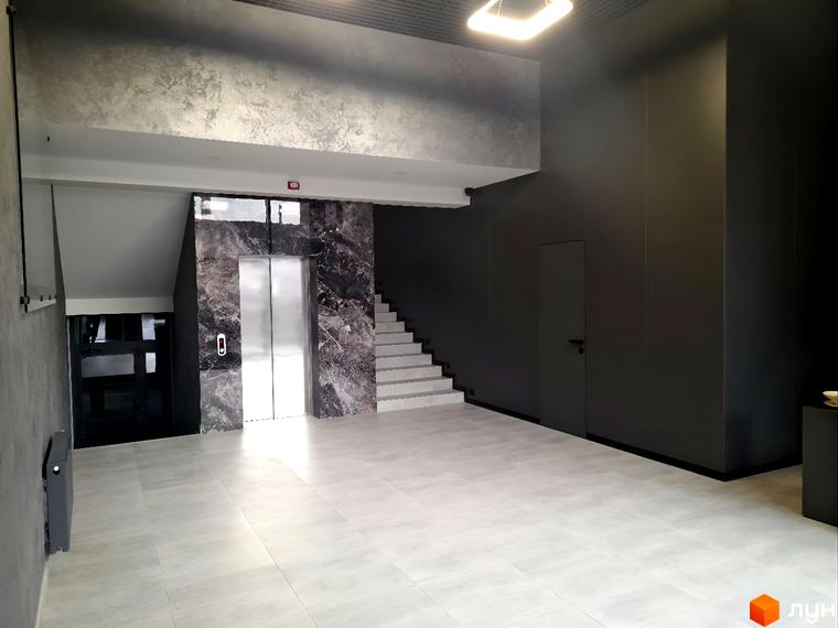 Сучасний хол житлового комплексу ONYX sweet home з ліфтом та сходами. Простір оформлений у темних тонах з акцентами на мармурову обробку.