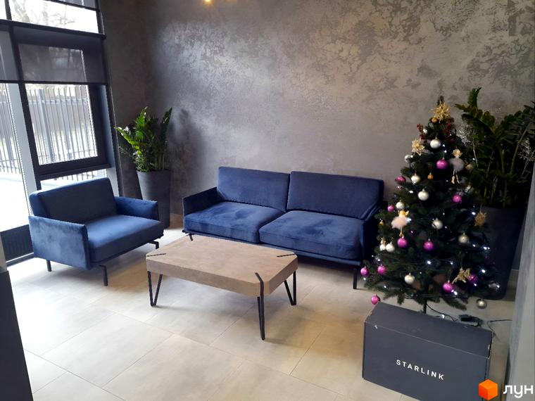 Затишна зона відпочинку з синіми диванами та кріслом біля кавового столика, прикрашена ялинкою. ONYX sweet home – ваш новий дім.