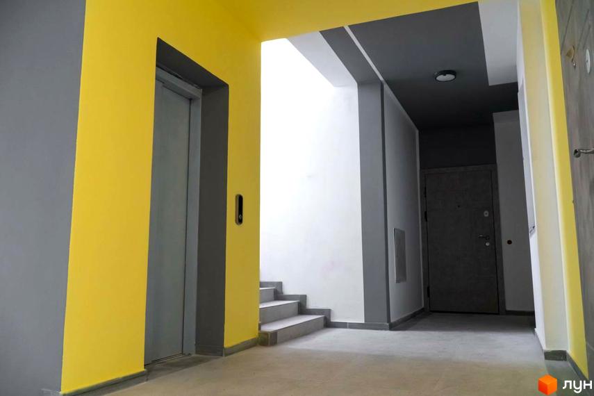 Інтер'єр під'їзду Житлового комплексу Зелені Пагорби: ліфт, сходи та двері до квартир, стіни у сірих та жовтих тонах.