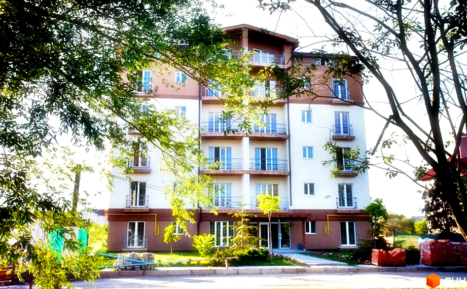 Житловий комплекс Бірюза - багатоповерховий будинок з балконами та великими вікнами. Навколо будинку зелена зона з деревами та квітковими клумбами.