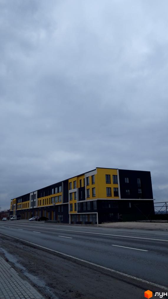 Новобудова на Підволочиському шосе з жовто-чорним фасадом та великою кількістю вікон. Поруч проходить дорога та тротуар.