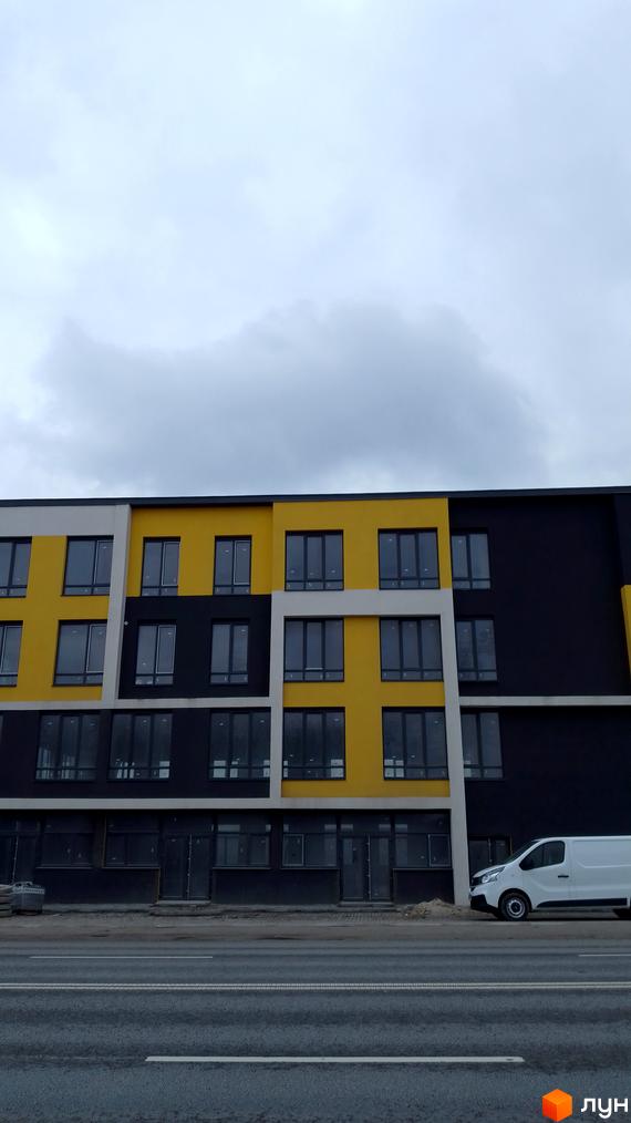 Фасад новобудови на Підволочиському шосе з жовтими, чорними та білими секціями. Поруч дорога та білий фургон.