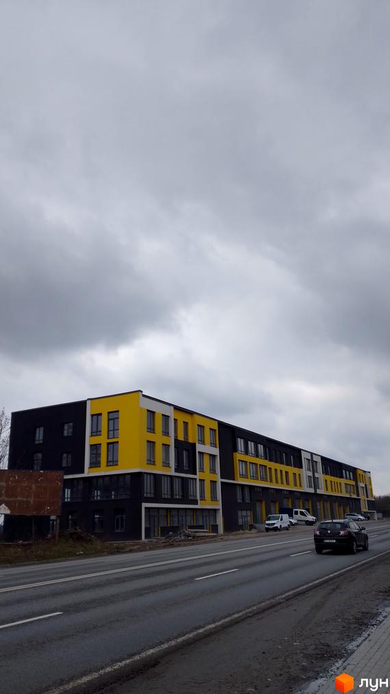 Житловий комплекс на Підволочиському шосе з яскравим жовто-чорним фасадом та великими вікнами. Поруч проходить дорога з автомобілями.
