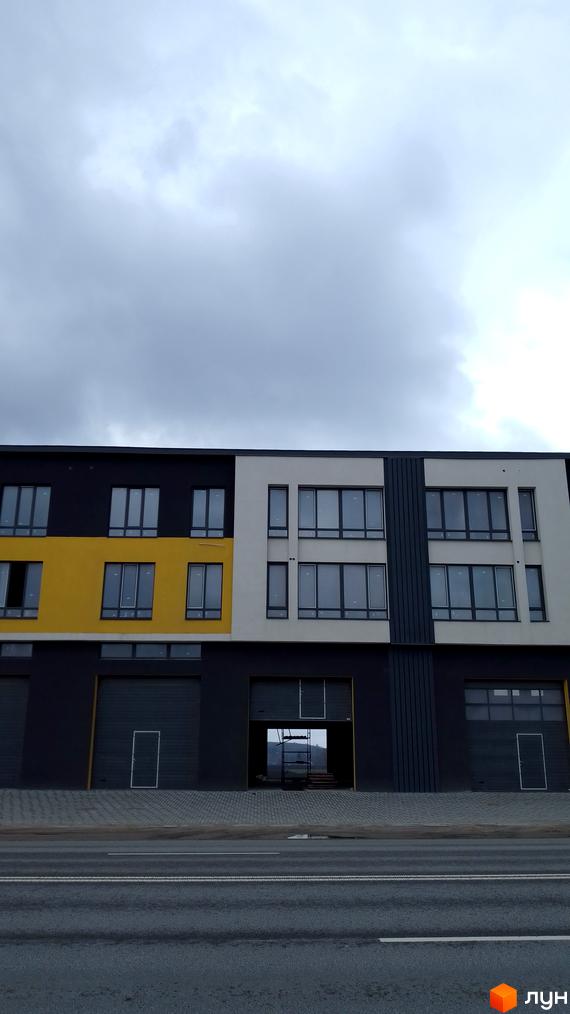 Фасад новобудови на Підволочиському шосе з великими вікнами та секціями різних кольорів. Зовнішній вигляд будівлі з гаражними воротами та входом.