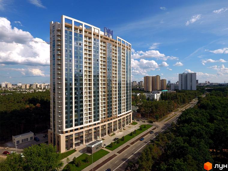 Житловий комплекс Автограф – висотна будівля зі скляним фасадом та балконами на тлі блакитного неба. Поруч дорога та зелені насадження.