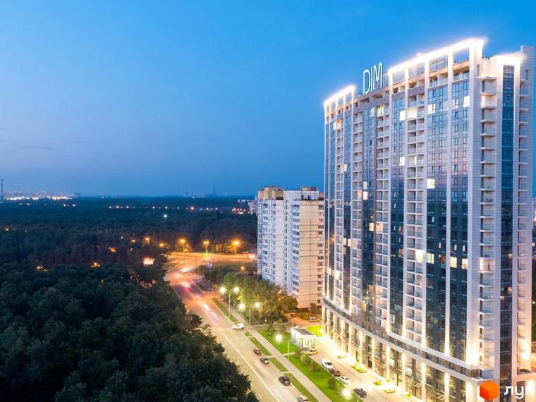 Новобудова ЖК Автограф з підсвіченим фасадом вночі. Навколо зелена зона та дорога з автомобілями.